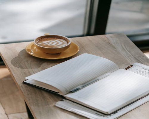 A warm cup of coffee next to open notebooks on a wooden table